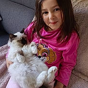 Plume participe au concours pour gagner de l'argent avec cette photo : child, girl, cat, pet, indoor, couch, blanket, smiling, long_hair, pink_clothing, fluffy_cat, relaxed, holding_pet, home, comfort, cute, young, seated, furniture, cozy