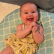 Charlotte is registered to the contest to win money with this photo: baby, smiling, happy, infant, clapping, yellow_dress, patterned_cushion, cute, cheerful, indoors, child, skin, face, arms, hands, joyful, seated, plush, clothing, expression