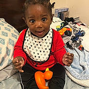 Dylan joined the competition — help win amazing prizes! toddler, child, baby, bed, blanket, pillow, toy, rubber_duck, clothing, red_shirt, black_pants, bib, smiling, indoors, person, cute, happy, hair, hand, sitting