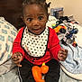 toddler, child, baby, bed, blanket, pillow, toy, rubber_duck, clothing, red_shirt, black_pants, bib, smiling, indoors, person, cute, happy, hair, hand, sitting