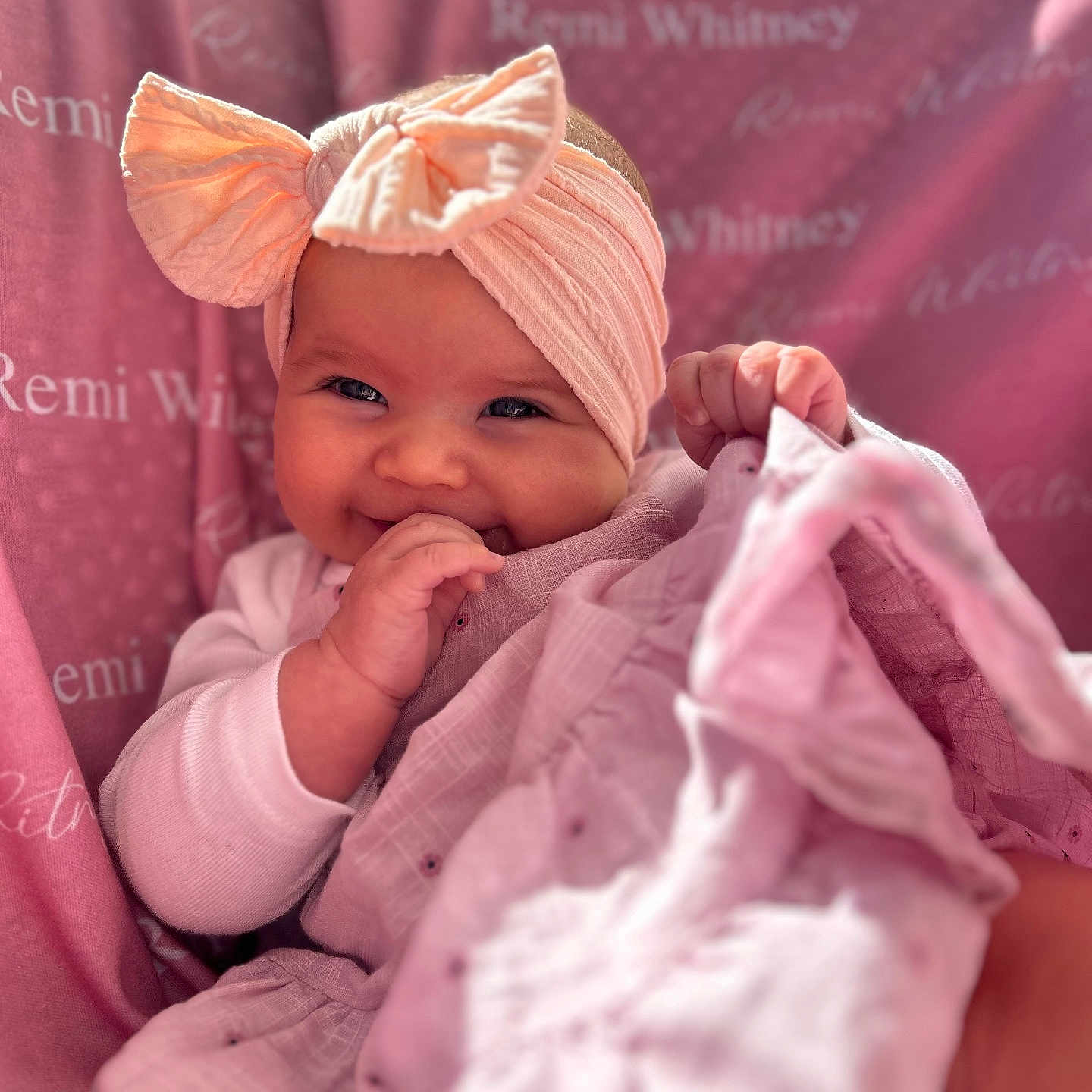 Remi joined the competition — help win amazing prizes! baby, blanket, bow, child, closeup, clothing, cozy, cute, face, happy, headband, indoors, infant, person, pink, portrait, sitting, smiling, soft, young