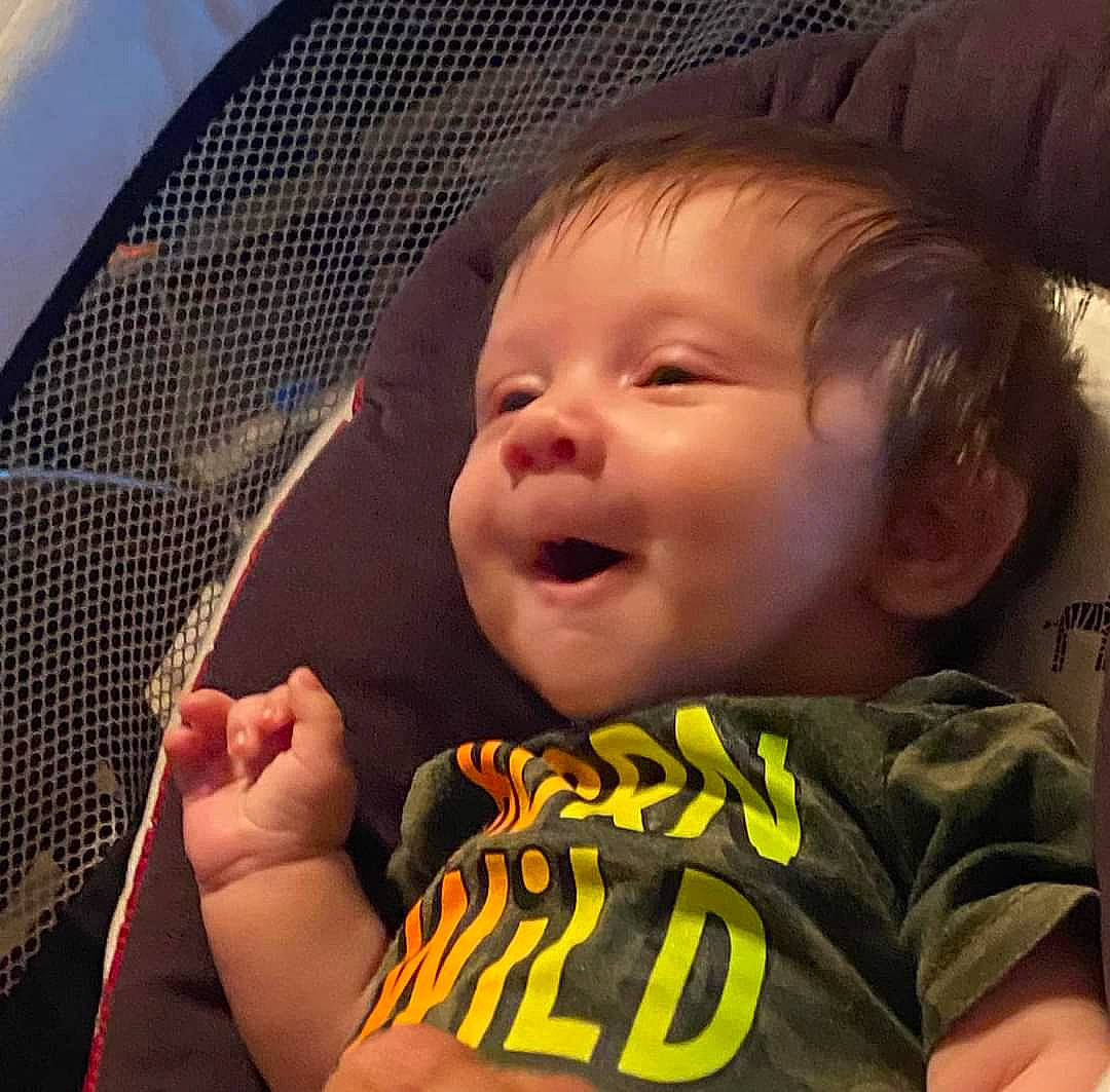 Bodhi is registered to the contest to win money with this photo: arm, baby, cheek, chin, comfort, eye, eyebrow, facial_expression, gesture, hairstyle, hand, happy, mammal, mouth, nose, person, product, skin, sleeve, smile