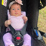 Celine is registered to the contest to win money with this photo: baby, infant, stroller, car_seat, headband, flower, pink_clothing, socks, straps, outdoor, grass, child, face, person, seatbelt, cute, young, portrait, sitting, expression