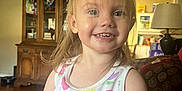 Riley is registered to the contest to win money with this photo: child, toddler, smiling, tank_top, colorful_clothing, indoor, living_room, furniture, cabinet, lamp, wood_floor, happy, cute, person, portrait, hair, face, eyes, arms, home