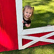 Riley joined the competition — help win amazing prizes! child, toddler, smiling, grass, outdoor, red_wood, white_wood, playful, happy, face, person, daylight, nature, shadow, wooden_structure, cute, young_child, peekaboo, sunlight, fun