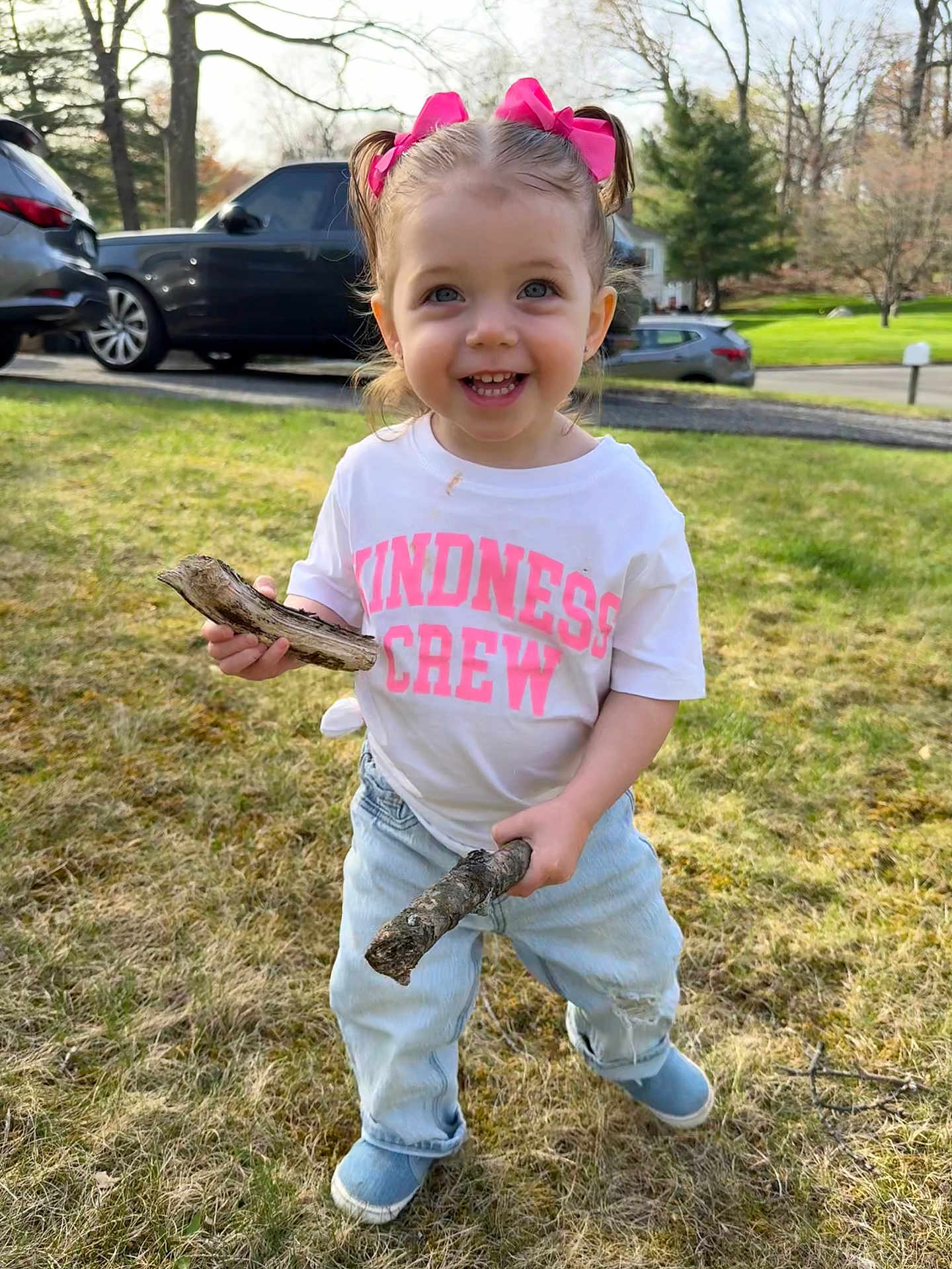 Sienna Mae joined the competition — help win amazing prizes! toddler, child, grass, outdoor, stick, pink_bow, jeans, white_shirt, smiling, happy, blue_eyes, pigtails, nature, daylight, car, tree, lawn, playful, person, casual_clothing