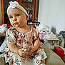Anna participe au concours pour gagner de l'argent avec cette photo : toddler, child, headband, flower, dress, sitting, indoor, furniture, cabinet, bottle, footwear, white, skin, person, young_child, cute, portrait, home, room, expression