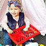toddler, child, blue_eyes, headband, floral, red_basket, toys, sitting, smiling, indoor, cute, happy, casual_clothing, jeans, white_shoes, playtime, floor, pink_backdrop, vest, candid