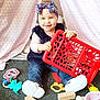 toddler, child, toys, red_basket, headband, vest, jeans, white_shoes, indoor, tent, pink_pattern, floor, blocks, teething_ring, smiling, sitting, playtime, baby, colorful, happy