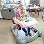 baby, walker, toy_car, striped_shirt, lacy_collar, navy_pants, hearts_pattern, socks, living_room, sofa, armchair, coffee_table, flooring, furniture, indoor, child, person, home, curious, seated
