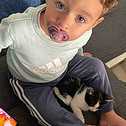 Loris a rejoint le concours — aidez-le/la à gagner de superbes lots ! toddler, child, pacifier, curly_hair, blue_eyes, kitten, cat, couch, clothing, sweatshirt, pants, hand, foot, smartphone, indoor, cozy, pet, sitting, looking_up, casual
