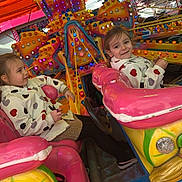 Hilona a rejoint le concours — aidez-le/la à gagner de superbes lots ! child, carnival, ride, amusement_park, colorful, lights, jacket, heart_pattern, outdoor, fun, smile, toy_car, seat, play, daylight, happy, festival, entertainment, person, family