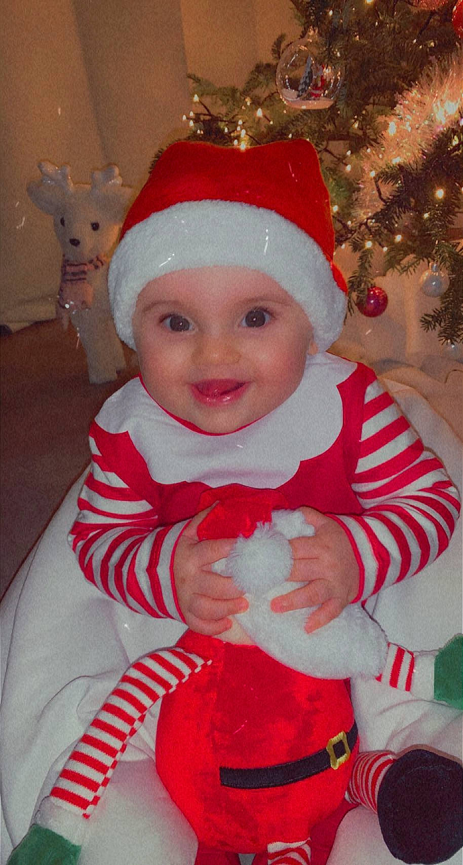 Asma participe au concours pour gagner de l'argent avec cette photo : baby, baby_toddler_clothing, cheek, child, christmas_tree, costume_hat, event, face, fictional_character, happy, head, headwear, holiday, joy, lap, person, pink, red, santa_claus, sleeve