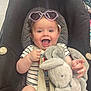 baby, child, car_seat, sunglasses, heart_shaped, stuffed_animal, bunny, toy, smiling, happy, clothing, striped_shirt, seatbelt, indoor, person, cute, infant, playful, young, portrait