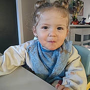 Romane participe au concours pour gagner de l'argent avec cette photo : toddler, child, messy, bib, sweater, table, indoor, face, smiling, hair_buns, person, eating, home, furniture, chair, expression, cute, young_child, portrait, curly_hair