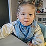 toddler, child, messy, bib, sweater, table, indoor, face, smiling, hair_buns, person, eating, home, furniture, chair, expression, cute, young_child, portrait, curly_hair