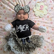 Allie is registered to the contest to win money with this photo: baby, infant, tutu, headband, black_shirt, slayer, leopard_print, mittens, socks, blanket, floral_pattern, wooden_sign, 2_months, smiling, lying_down, cute, child, clothing, person, indoor