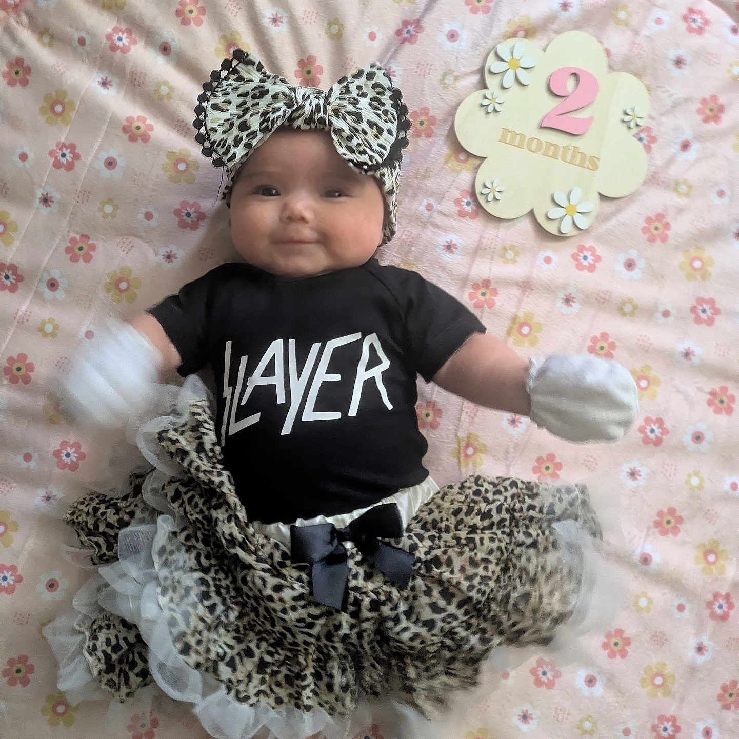 Allie is registered to the contest to win money with this photo: 2_months, baby, black_shirt, blanket, child, clothing, cute, floral_pattern, headband, indoor, infant, leopard_print, lying_down, mittens, person, slayer, smiling, socks, tutu, wooden_sign