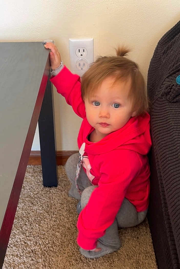Belladonna June is registered to the contest to win money with this photo: child, toddler, baby, red_hoodie, hoodie, carpet, table, couch, outlet, wall, sitting, squatting, hand_on_table, blue_eyes, brown_hair, pony_tail, indoor, living_room, cute, casual_clothing