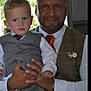 child, man, toddler, suit, vest, tie, formal_wear, portrait, indoor, holding, blue_eyes, short_hair, beard, smiling, person, fashion, family, event, closeup, hands