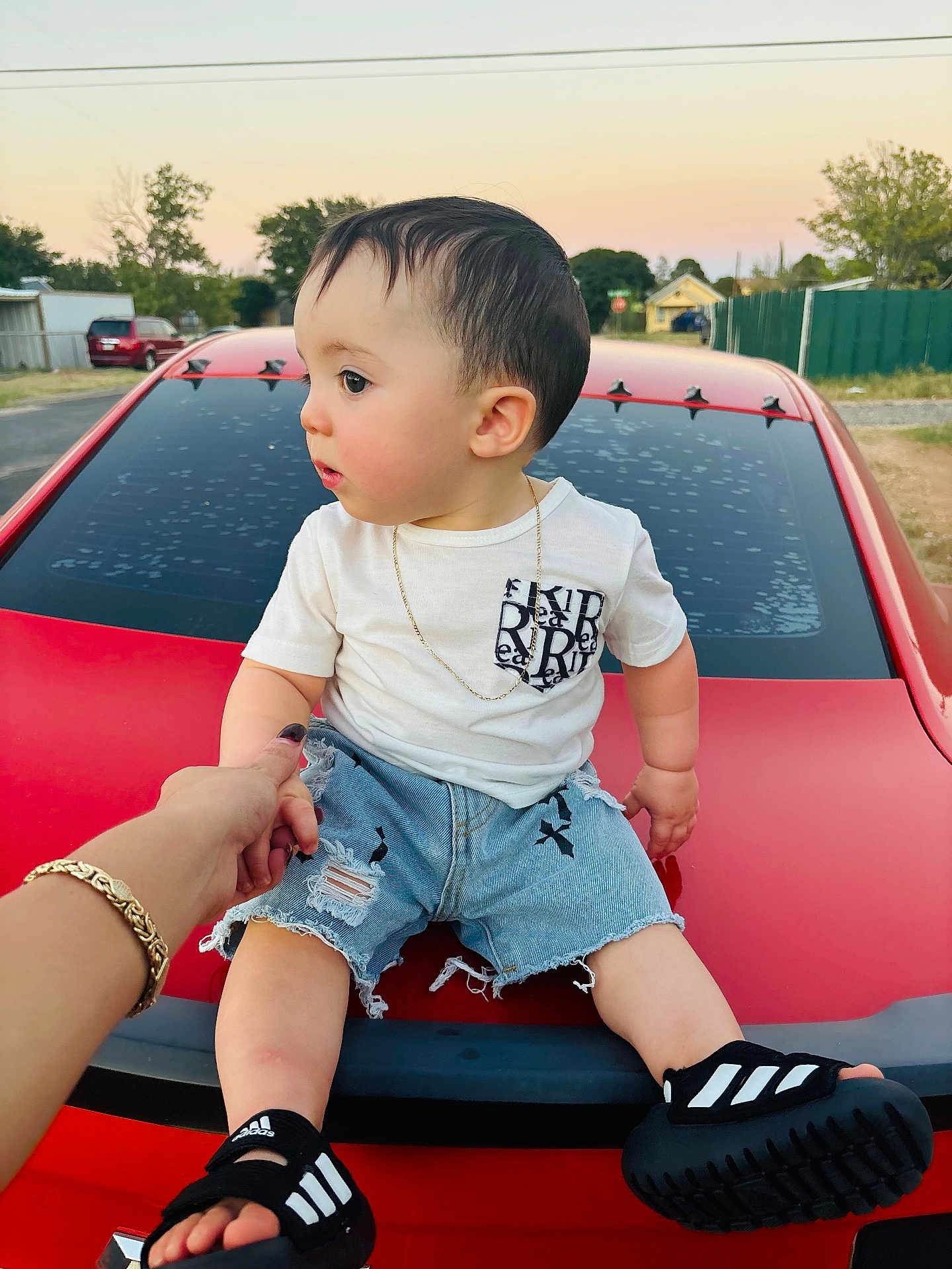Thiago Gael is registered to the contest to win money with this photo: adult_hand, black_sandals, casual_clothing, child, curious, denim_shorts, footwear, gold_bracelet, holding_hand, necklace, outdoor, red_car, shorts, side_view, street, suburban, summer, sunset, toddler, white_tshirt