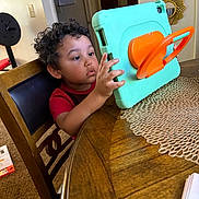 Jaxton joined the competition — help win amazing prizes! child, curly_hair, tablet, protective_case, wooden_table, placemat, chair, home, indoor, person, technology, curiosity, young, sitting, furniture, red_shirt, carpet, doorway, mirror, hand