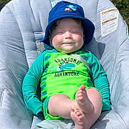 Saint is registered to the contest to win money with this photo: baby, baseballcap, cap, chair, clothing, coat, cushion, face, furniture, grass, hat, head, jacket, pants, person, photography, plant, portrait, sitting, t_shirt