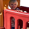 Michael is registered to the contest to win money with this photo: child, toddler, playground, smiling, outdoor, plastic_structure, red, yellow, green, sunlight, happy, short_hair, casual_clothing, daytime, play, fence, nature, person, young_child, play_area