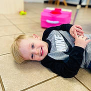 Michael joined the competition — help win amazing prizes! child, boy, smiling, lying_down, floor, tile_floor, blonde_hair, nike, sweatshirt, long_sleeve, indoor, toy, pink_toy, background_blur, happy, casual_clothing, portrait, person, young, cute