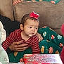 baby, child, red_bow, striped_shirt, hand, couch, christmas_presents, gift_wrap, holiday_pajamas, feet, person, indoor, festive, celebration, curious, portrait, family, support, cozy, seasonal