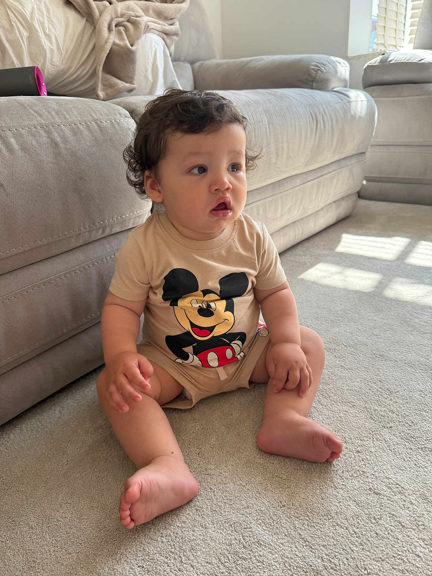 Jacobie is registered to the contest to win money with this photo: baby, carpet, child, comfortable, couch, curly_hair, cute, expression, indoor, living_room, mickey_mouse, natural_light, onesie, person, plush, sitting, sofa, soft, toddler, young_child