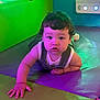 Jacobie joined the competition — help win amazing prizes! baby, child, colorful_mat, crawling, curly_hair, cute, expression, eyes, face, floor, green_lighting, hands, indoor, infant, overalls, person, play_area, purple_lighting, white_shirt, young_child