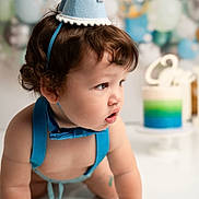 Jacobie is registered to the contest to win money with this photo: baby, blue, party_hat, birthday, cake, balloons, crawling, suspenders, bow_tie, curly_hair, celebration, first_birthday, face, child, indoor, decorations, colorful, white_background, cute, portrait