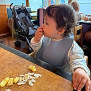 Jacobie joined the competition — help win amazing prizes! baby, bib, casual_clothing, child, curly_hair, daylight, eating, face, focused, food, hand, high_chair, indoor, person, restaurant, stroller, table, toddler, window, wooden_table