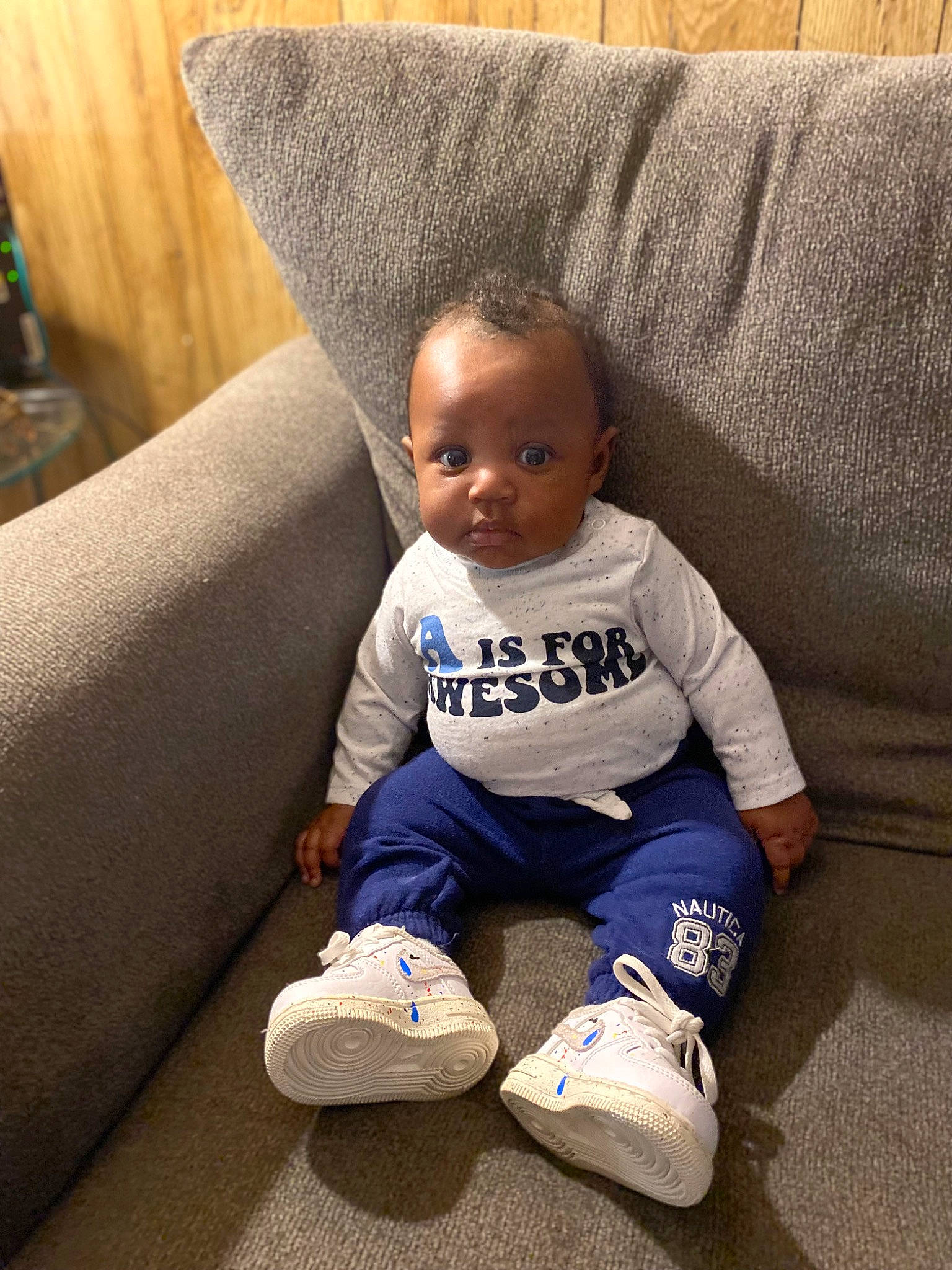 Ashton is registered to the contest to win money with this photo: baby, baby_toddler_clothing, comfort, couch, flooring, head, human_body, knee, leg, living_room, person, pillow, sleeve, smile, sneakers, sock, sportswear, t_shirt, textile, toddler
