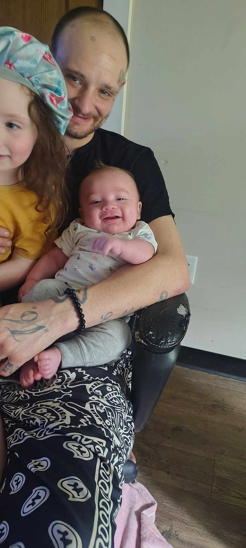 Storm joined the competition — help win amazing prizes! man, baby, child, toddler, smiling, hat, tattoo, bracelet, armchair, onesie, pants, wood_floor, indoor, portrait, holding, happy, curly_hair, seat, clothing, face