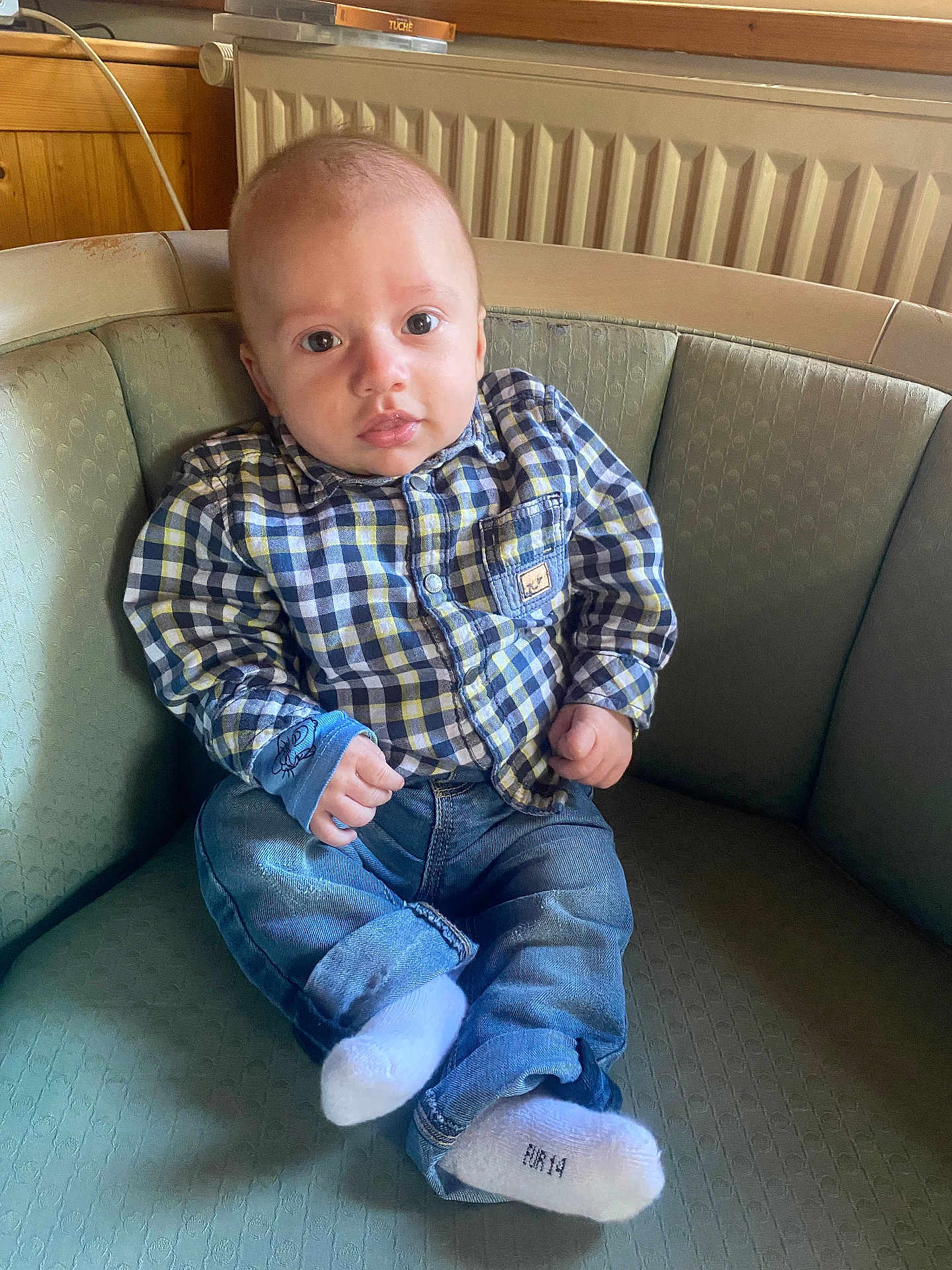 Malone participe au concours pour gagner de l'argent avec cette photo : baby, child, infant, plaid_shirt, jeans, socks, couch, furniture, indoors, radiator, wood_paneling, face, person, seated, curious, casual_clothing, home, portrait, young_child, comfortable