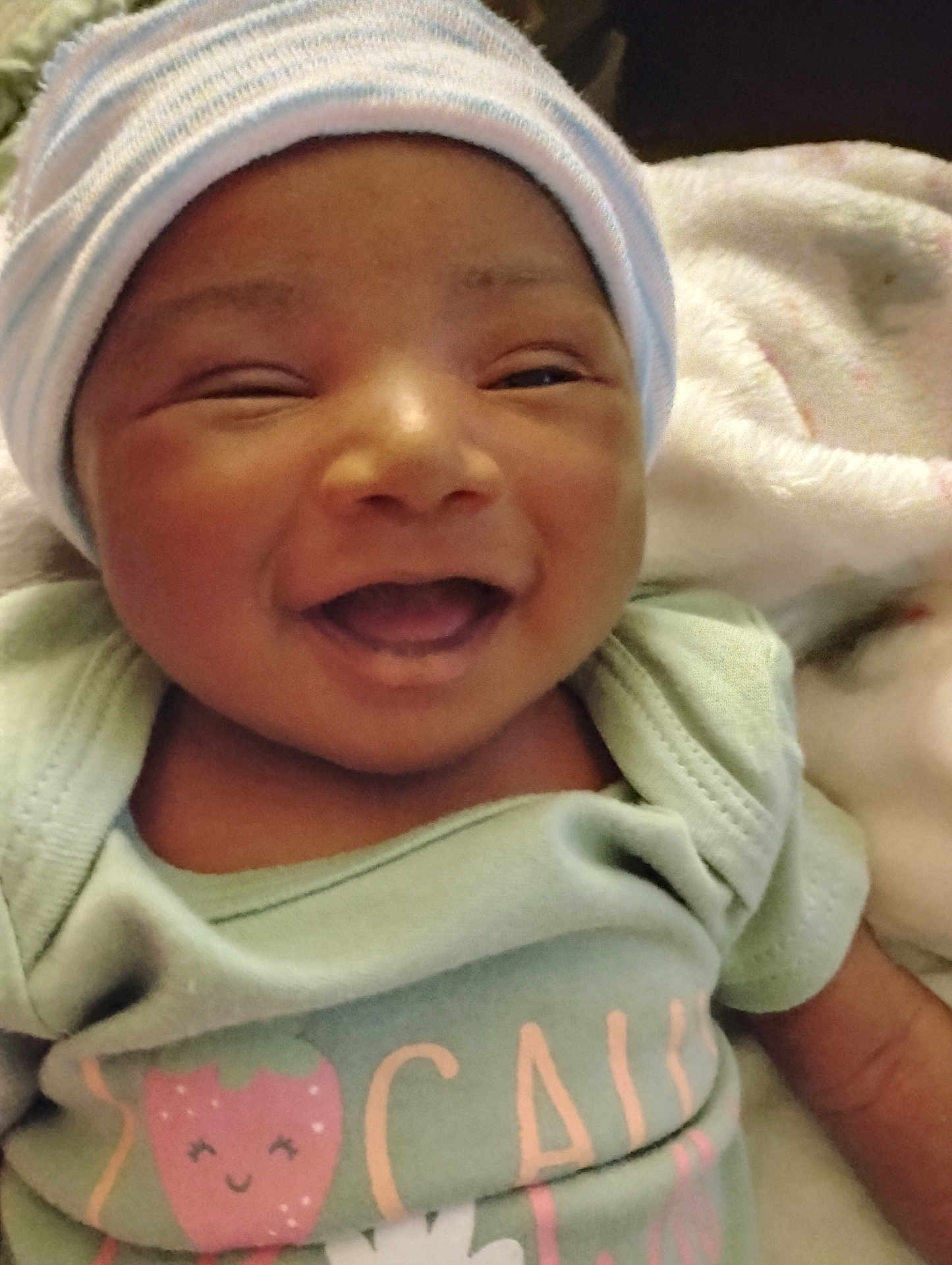 Divine is registered to the contest to win money with this photo: baby, smiling, hat, onesie, blanket, happy, infant, face, cute, child, apparel, sleepwear, portrait, lying_down, newborn, closeup, expression, cheerful, soft, cozy