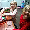 Major is registered to the contest to win money with this photo: child, smiling, birthday, cake, present, unwrapping, kitchen, table, adult, portrait, family, celebration, colorful, food, frosting, gift_wrap, countertop, indoors, red_shirt, happy