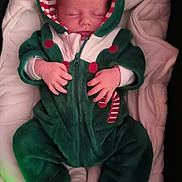 Tiago participe au concours pour gagner de l'argent avec cette photo : baby, sleeping, onesie, hood, blanket, infant, cozy, red_buttons, candy_cane, green_clothing, white_blanket, soft_fabric, newborn, hands, peaceful, cute, portrait, indoors, child, warm