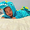 Niklaus is registered to the contest to win money with this photo: baby, child, dinosaur_costume, blue, turquoise, smiling, happy, portrait, indoor, bed, blanket, bedroom, infant, costume, hood, playful, lying_down, face, adorable, photography