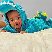 Niklaus joined the competition — help win amazing prizes! baby, child, infant, dragon_costume, turquoise, hood, smiling, happy, face, portrait, indoor, bedroom, bed, white_bedding, lying_down, playful, costume, dinosaur, photography, cute