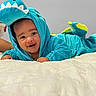 baby, child, infant, dragon_costume, turquoise, hood, smiling, happy, face, portrait, indoor, bedroom, bed, white_bedding, lying_down, playful, costume, dinosaur, photography, cute