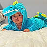 Niklaus joined the competition — help win amazing prizes! baby, child, dinosaur_costume, dinosaur_hood, blue, green, costume, cute, portrait, face, eyes, indoors, bed, bedding, lying_down, infant, playful, soft_toy, photography, smiling