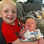 Myles is registered to the contest to win money with this photo: child, baby, toddler, smile, red_shirt, onesie, blond_hair, couch, pillow, blanket, indoor, holding, happy, infant, person, furniture, family, casual_clothing, home, cute