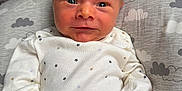 Louis joined the competition — help win amazing prizes! baby, newborn, infant, onesie, stars, white_clothing, face, eyes, smile, cushion, cloud_pattern, soft_fabric, hand, skin, portrait, indoors, closeup, child, cute, resting