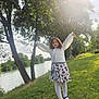 child, girl, outdoor, river, trees, grass, sunlight, white_tights, black_shoes, floral_skirt, long_sleeve, purse, nature, greenery, smiling, happy, pose, daylight, park, scenic