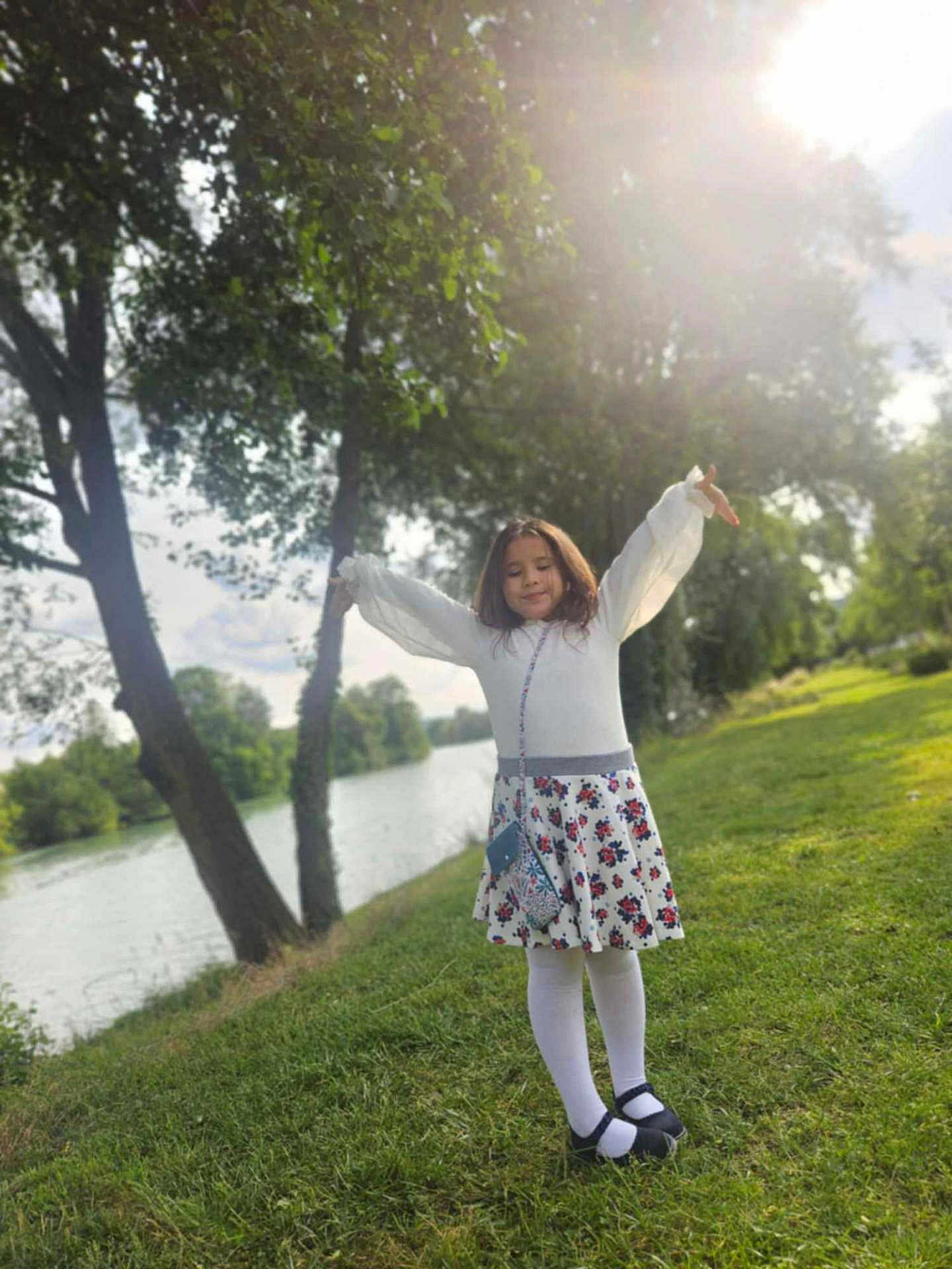 élae a rejoint le concours — aidez-le/la à gagner de superbes lots ! child, girl, outdoor, river, trees, grass, sunlight, white_tights, black_shoes, floral_skirt, long_sleeve, purse, nature, greenery, smiling, happy, pose, daylight, park, scenic