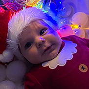 Toby joined the competition — help win amazing prizes! baby, child, santa_hat, christmas, holiday, festive, red_outfit, lights, decorations, white_balls, face, portrait, cute, infant, smile, cozy, soft_lighting, indoor, celebration, seasonal