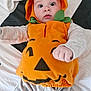Walter is registered to the contest to win money with this photo: baby, pumpkin_costume, orange, cute, infant, child, bed, blanket, clothing, costume, expression, face, hand, hood, indoor, lying_down, person, playful, smile, young
